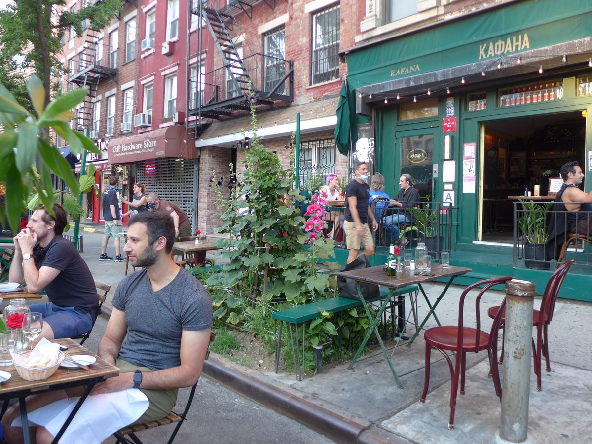 A sidewalk cafe showing a few people relaxing at tables in parking spots in the street.