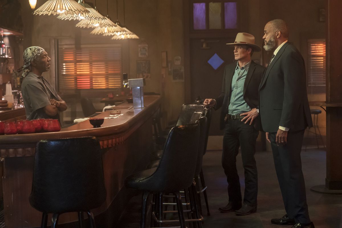 Sweety (Vondie Curtis-Hall) stands behind his bar with his arms folded and talks to Raylan Givens (Timothy Olyphant) and his partner
