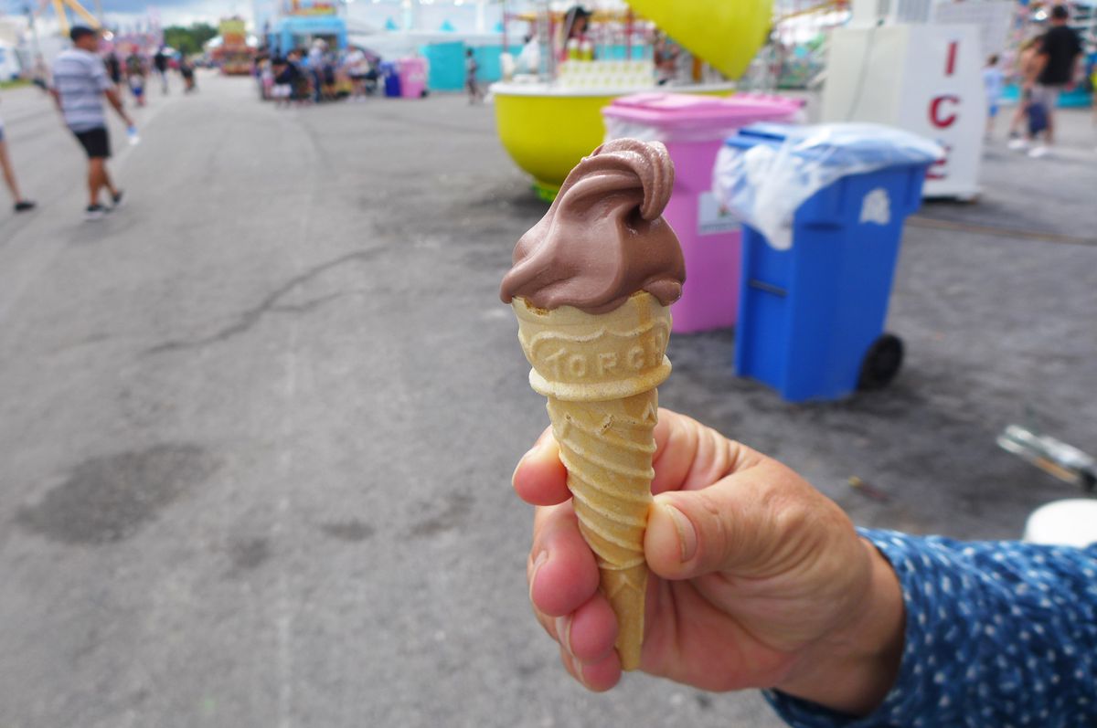 A hand holds out a tiny chocolate ice cream cone.