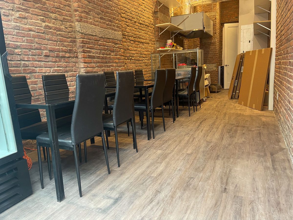 A narrow, brick-walled dining room with black tables and chairs set up along the left side.