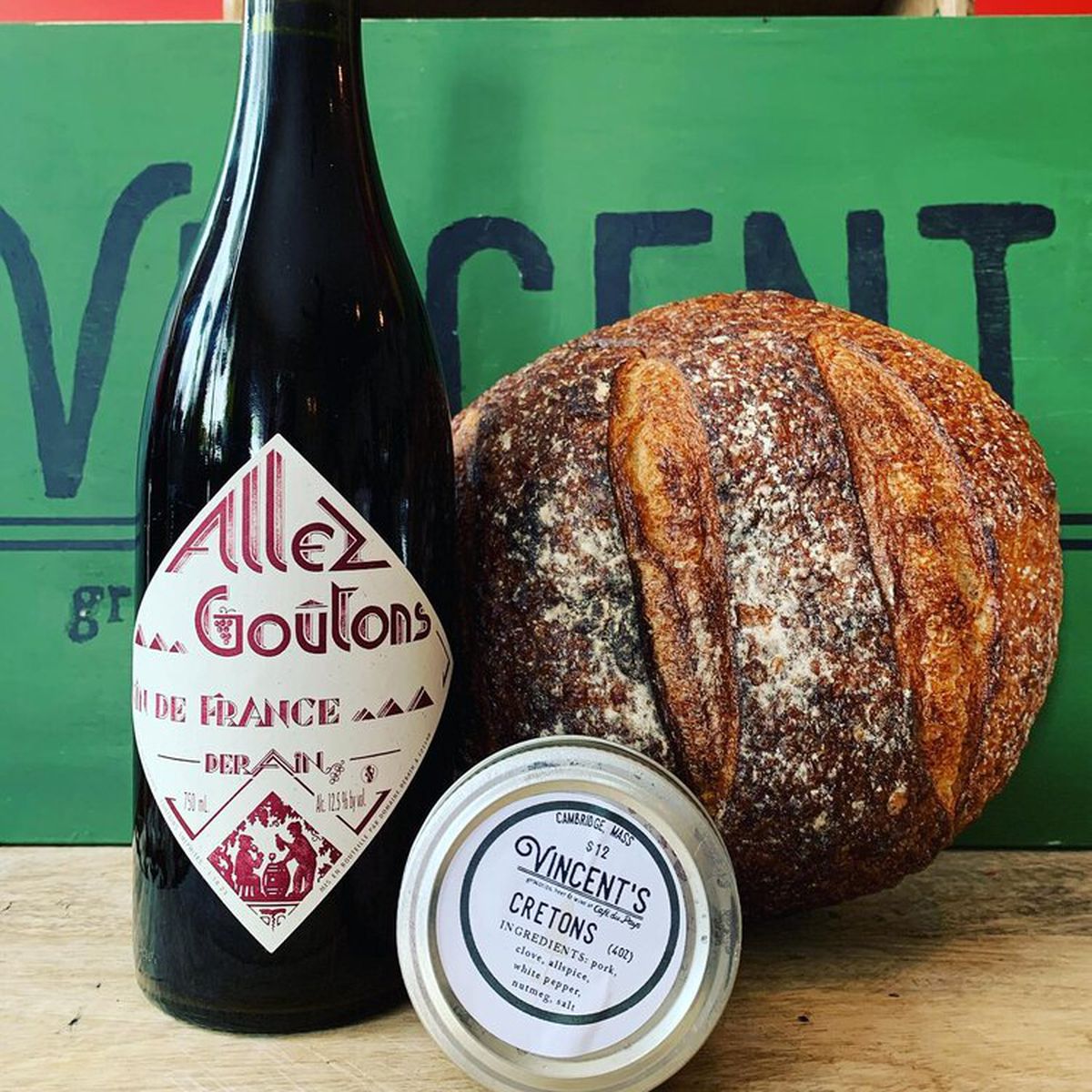 A wine bottle and fresh loaf of bread in front of a green sign that says Vincent’s