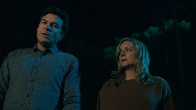 jason bateman and laura linney stand side by side in darkness. she looks up at him