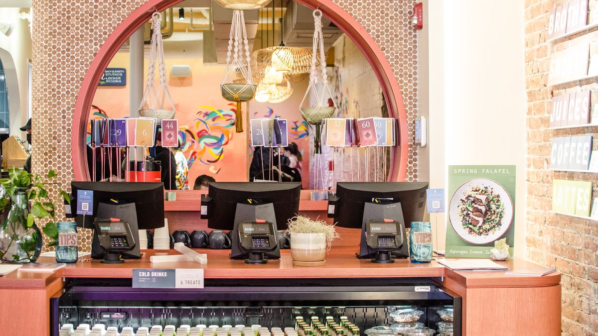 The registers at a fast-casual chain with bright, colorful decor, lots of exposed brick, and bottles of fresh juices.