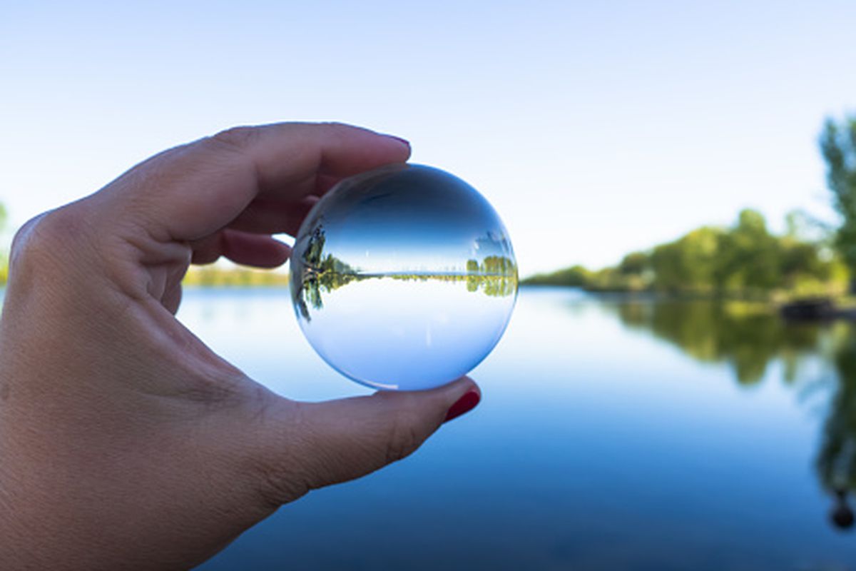 A woman with a crystal ball in her hand showing a reflection of a river and blue sky.