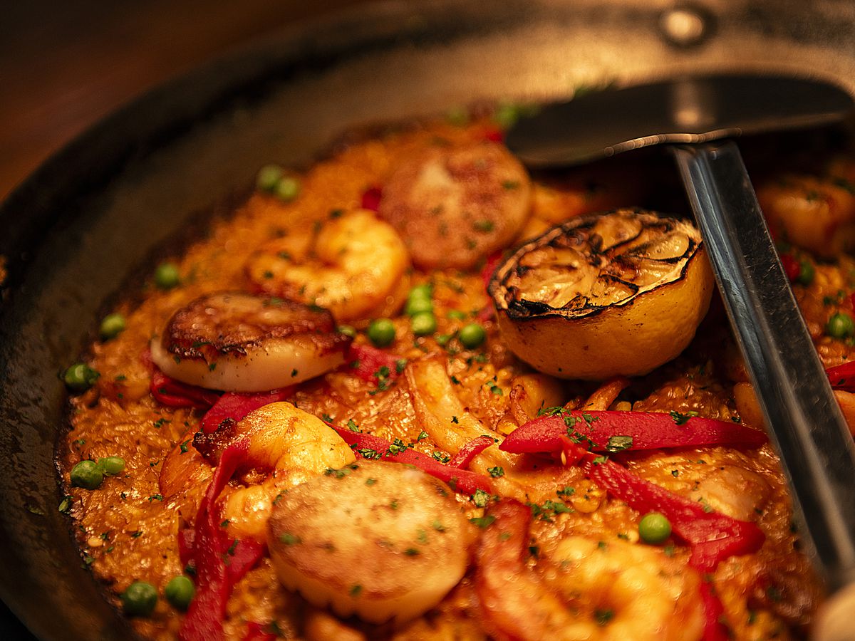 A close up of paella with shrimp, scallops, lemon, and other ingredients.