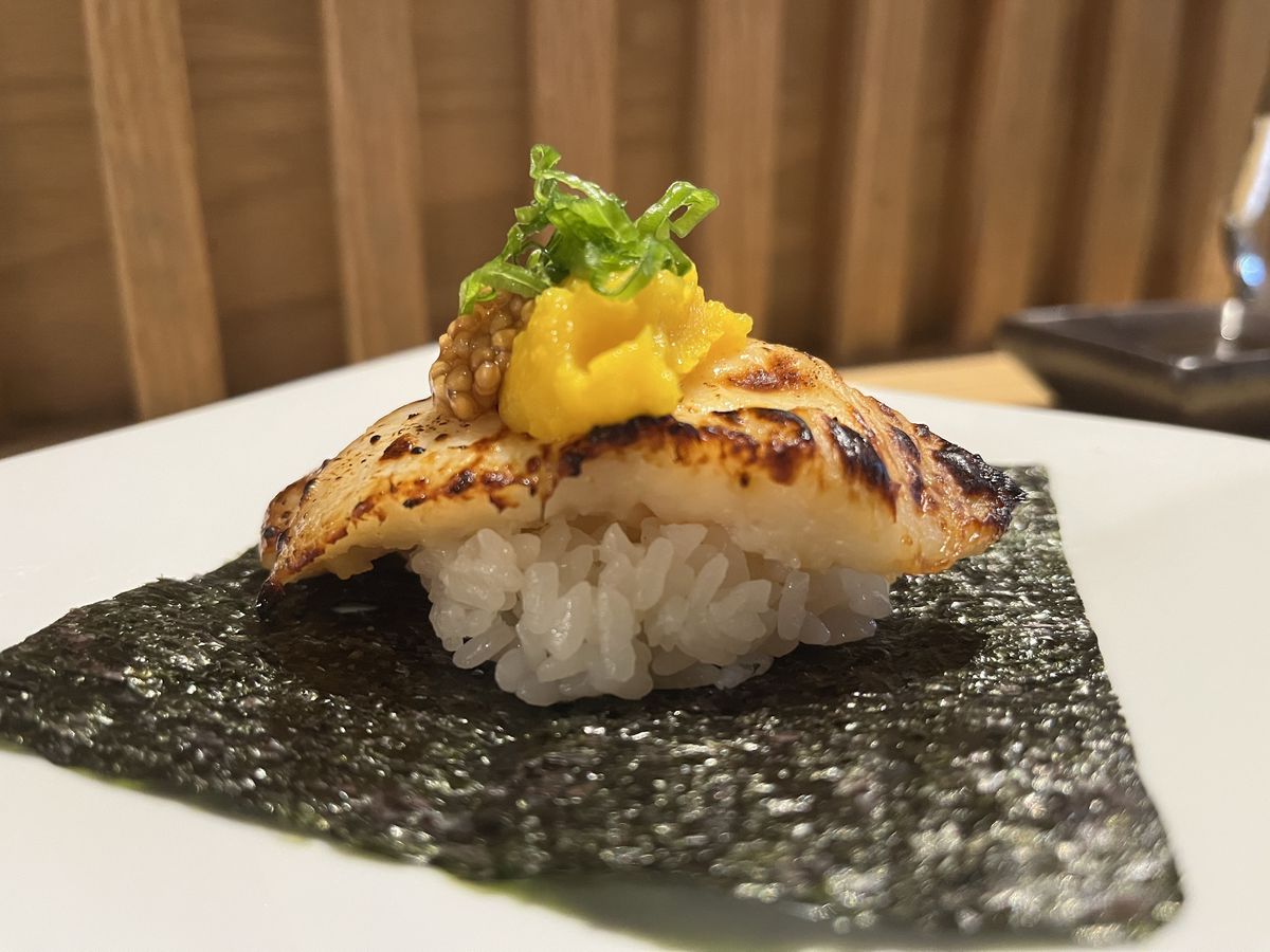 A sushi handroll with a piece of blackened cod layered over a scoop of rice on top of a seaweed square.