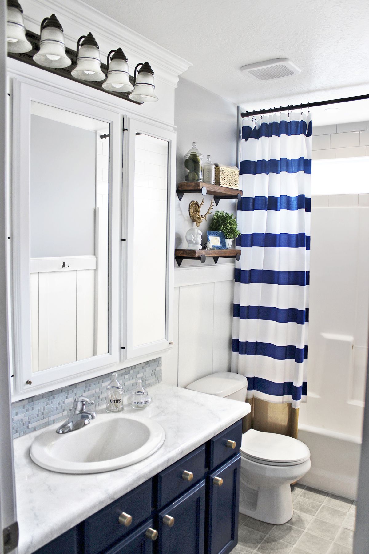 <p><strong>After:</strong> A capacious medicine cabinet and more shelving in the vanity help keep things organized; simple wainscoting and a stylish navy, gray, and white palette give the space loads more personality.</p>