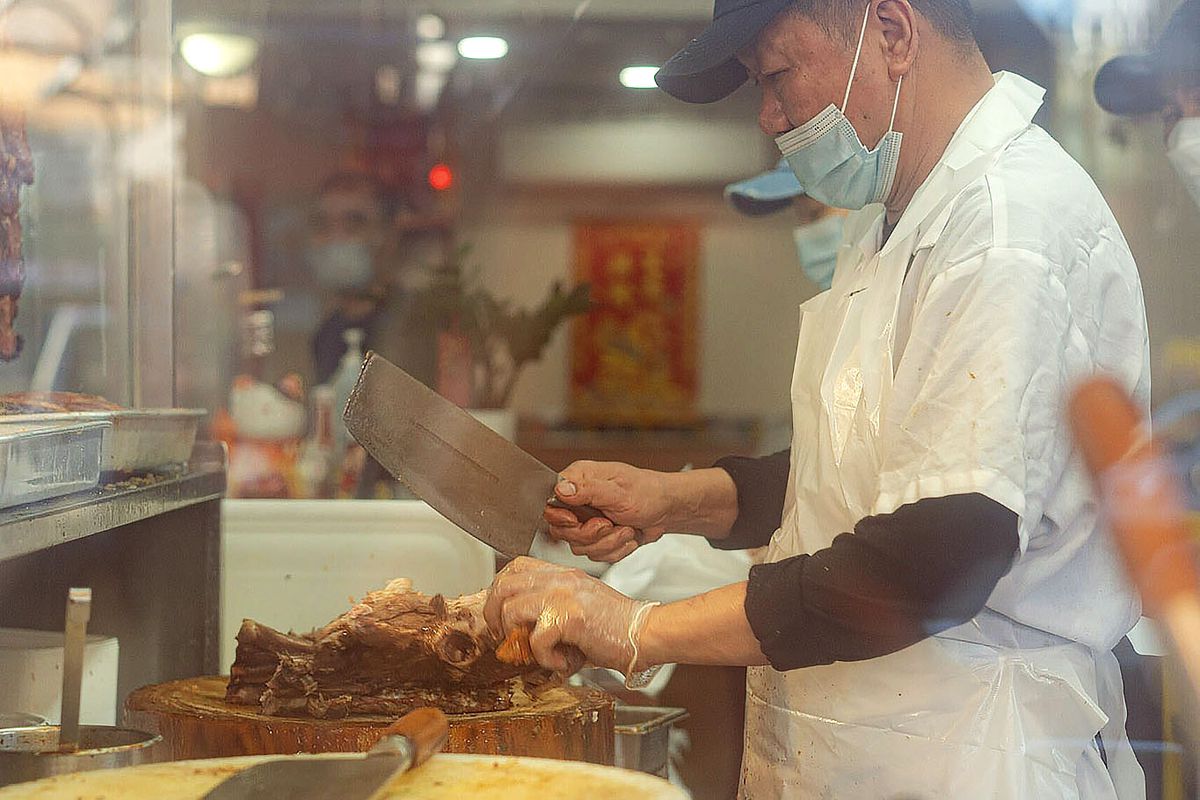 A masked man with a clever cuts into Chinese barbecue.