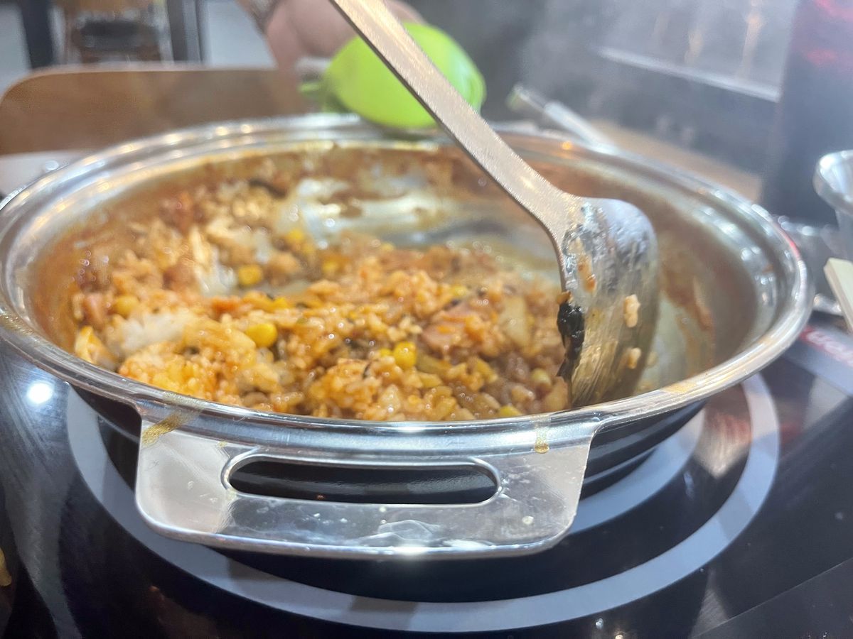 A person stirs fried rice on a bowl atop a table burner at Bellaire’s Dookki Tteokbokki.
