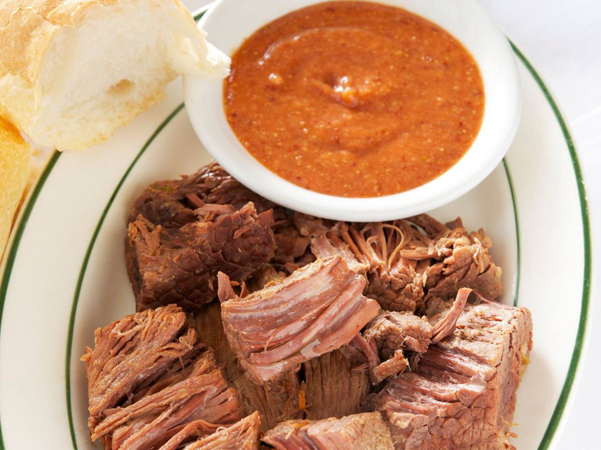 A plate with shredded boiled beef brisket served with a red sauce and baguette bread