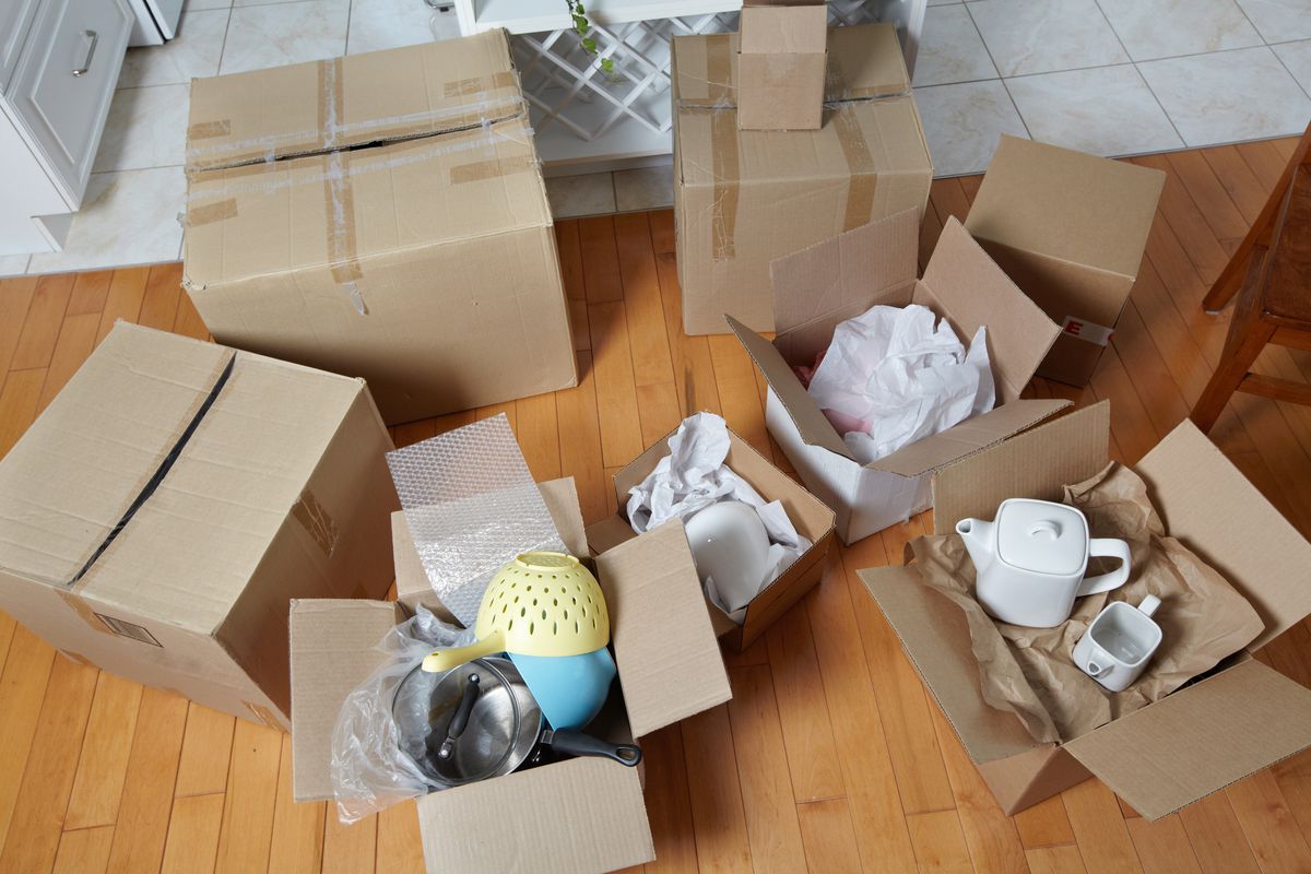 Assorted cardboard moving boxes on the floor with dishes and packing paper.