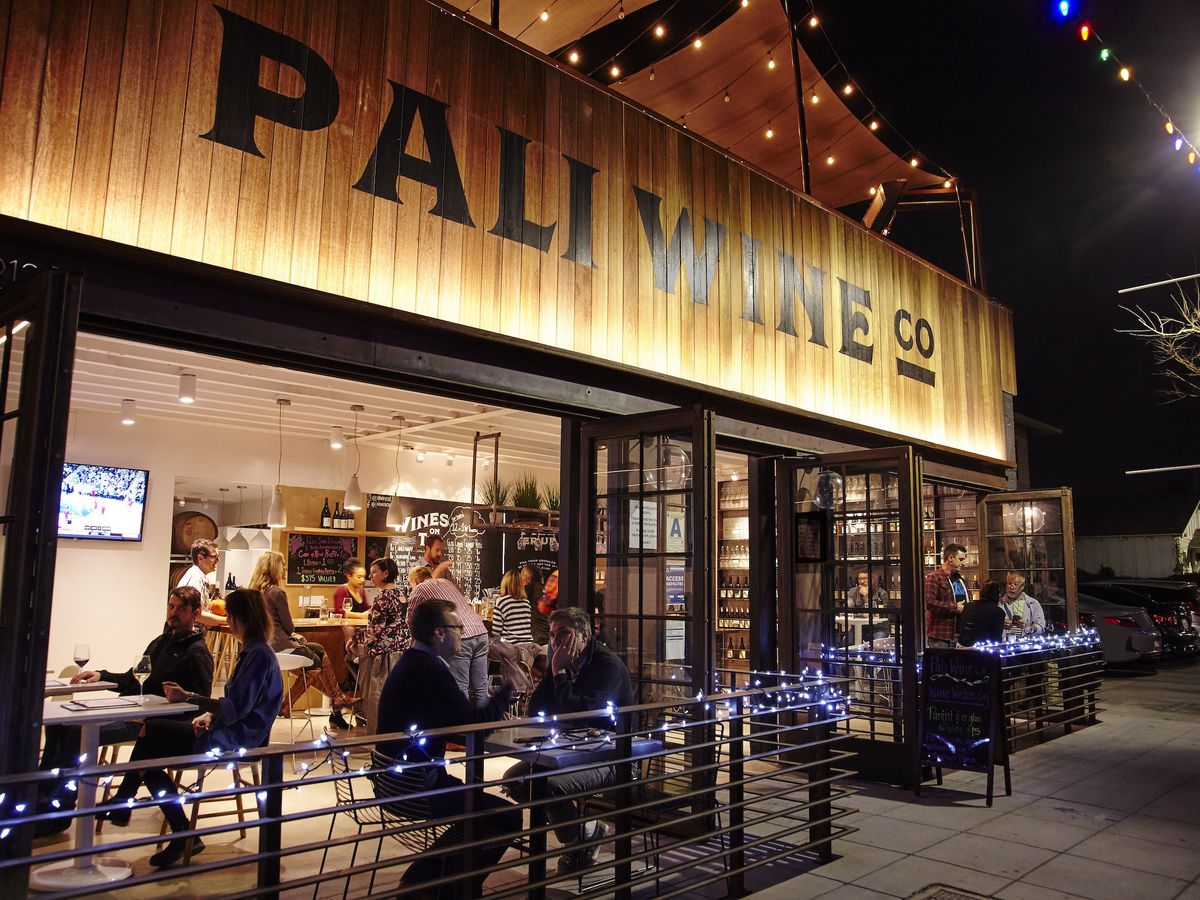 People sitting on the front patio of Pali Wine Co. at night.