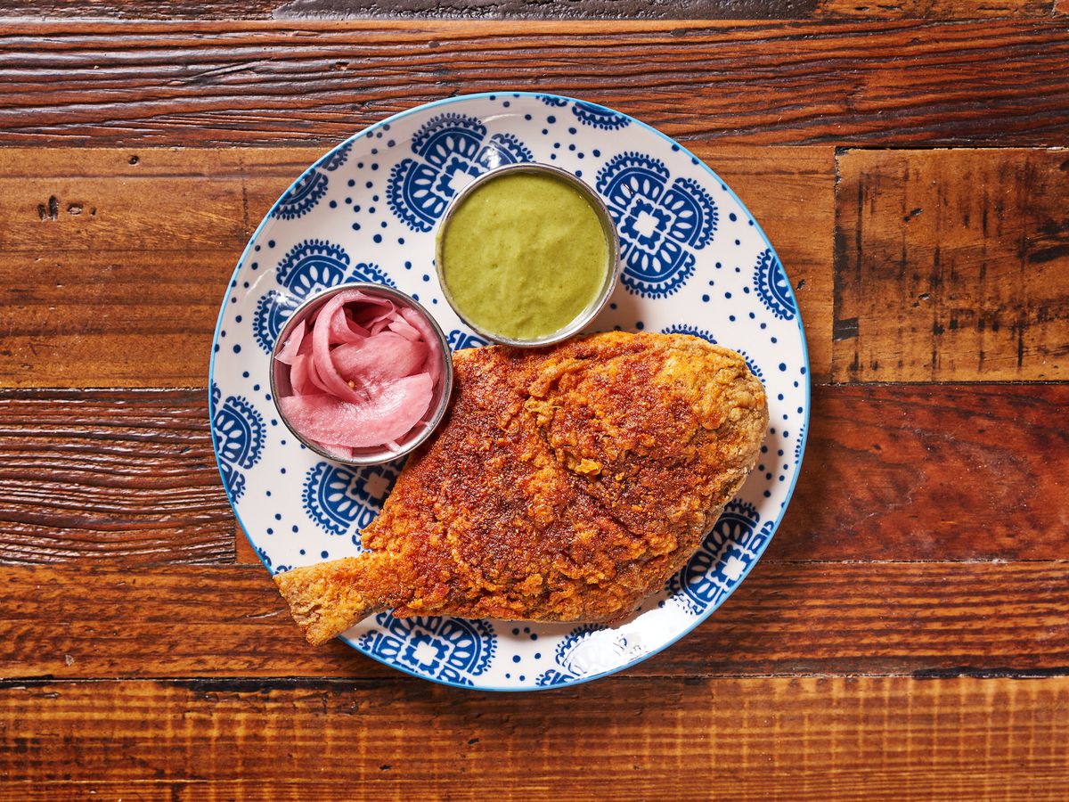 A whole fried fish placed on a blue plate next to a green sauce