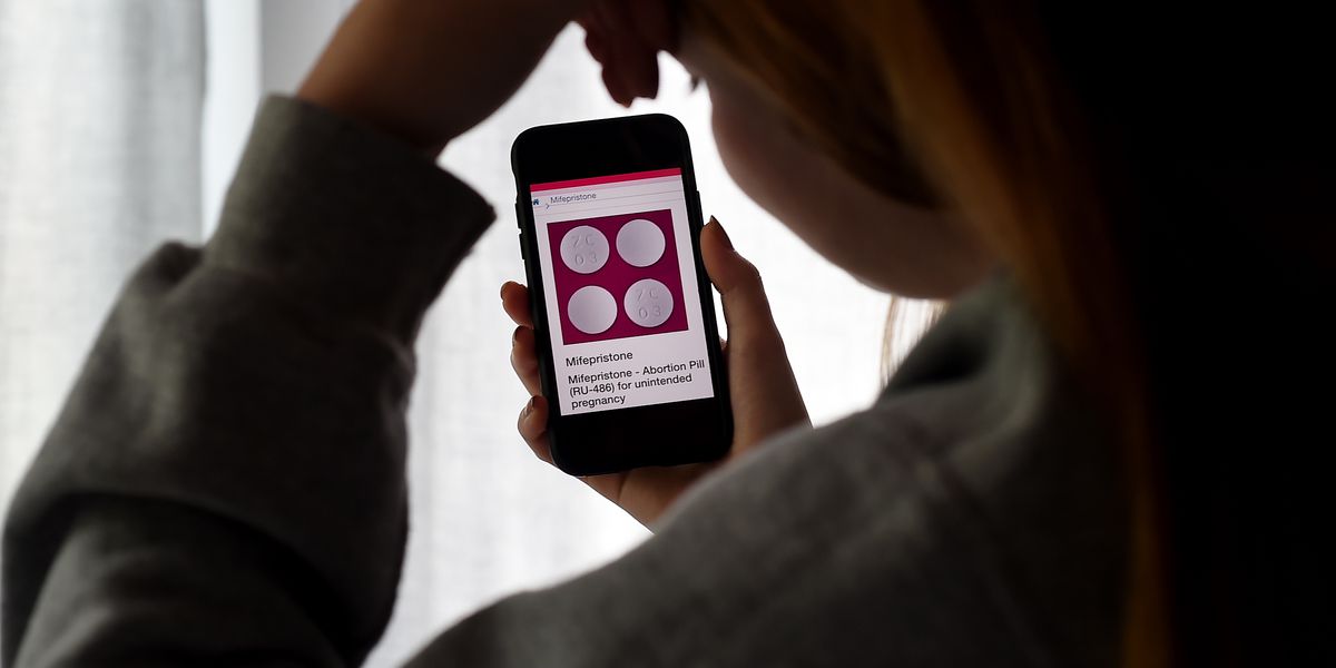 In this photo illustration, a person looks at an abortion pill displayed on a smartphone