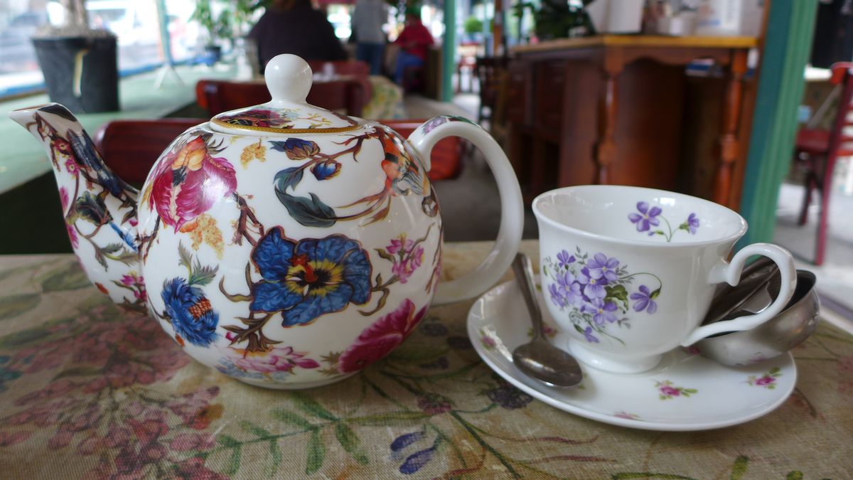 A flowered tea pot with a matching teacup on the side.