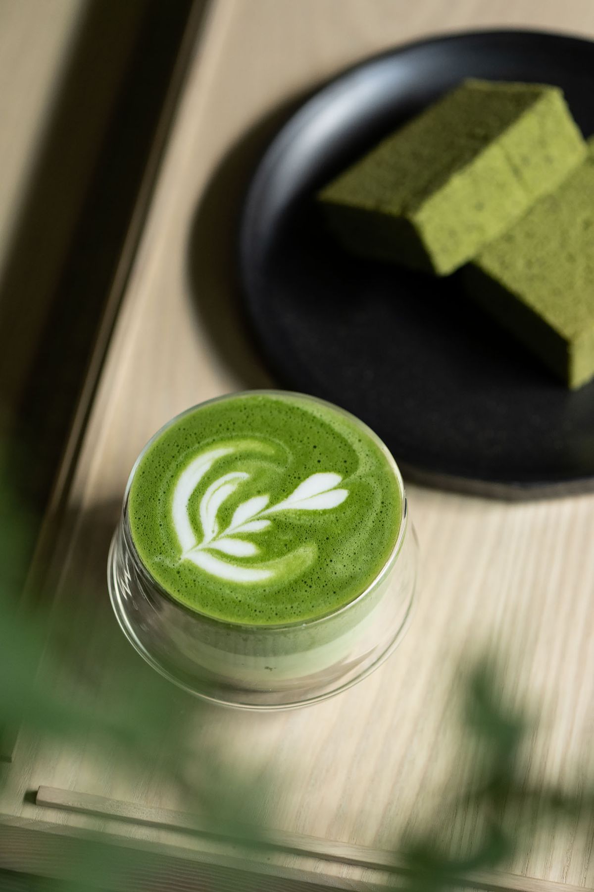 A green matcha latte with matcha cake on a wooden bench.