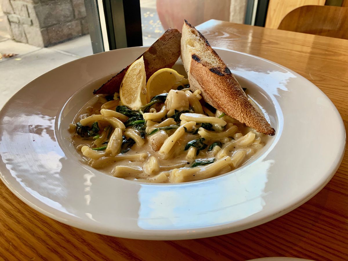 A white place with pasta mixed with a creamy lemon and spinach sauce topped with lemon slices and spears of garlic bread