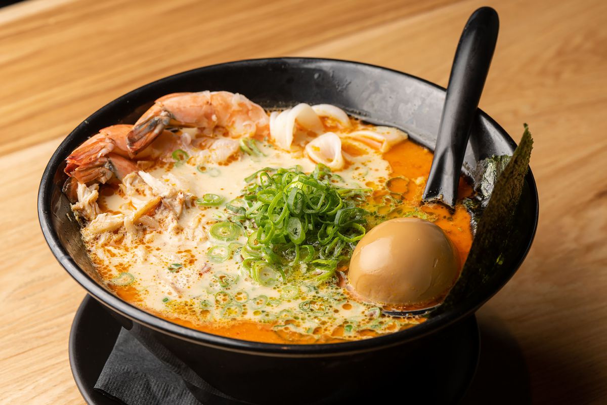 A wide shot of an orange soup with noodles and a tan egg.