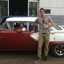 This May 15, 2015 photo shows Mario Otero in front of a classic American car driven by his friend Camilo Rodriguez in Havana, Cuba. Otero, 25, works as a waiter in one of Havana's best restaurants, has a tourism degree, moonlights as a private tour guide with a goal of someday opening his own tourism agency, and sees increased tourism in Cuba as a key to achieving his dreams. Otero, who speaks English and French, is also renovating a house he hopes to rent to tourists. 