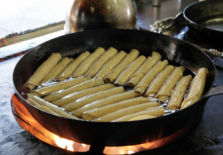 Rolled taquitos in a cast iron skillet over a fire.