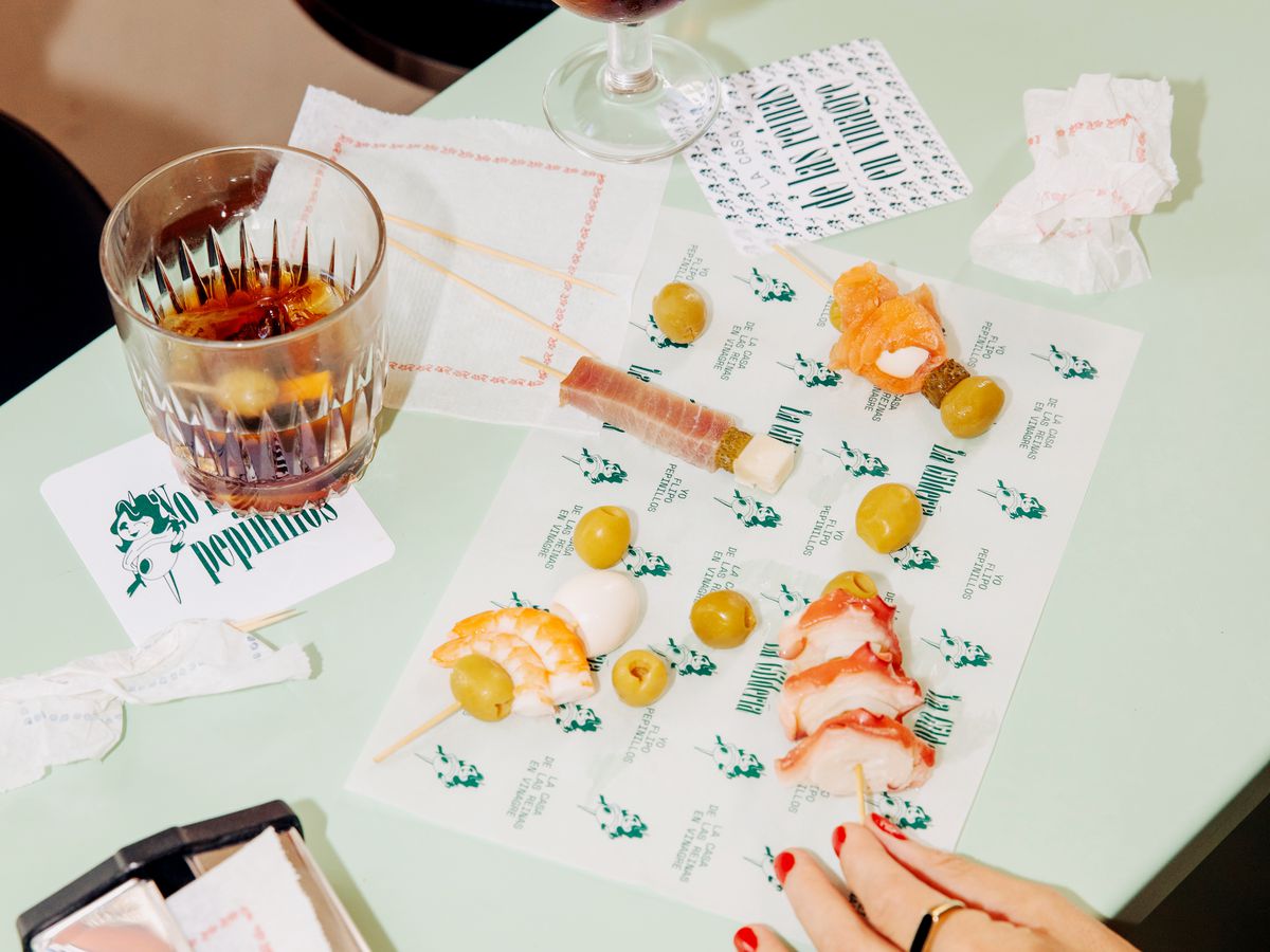 People pick at skewered snacks on a branded placemat while drinking glasses of sherry.