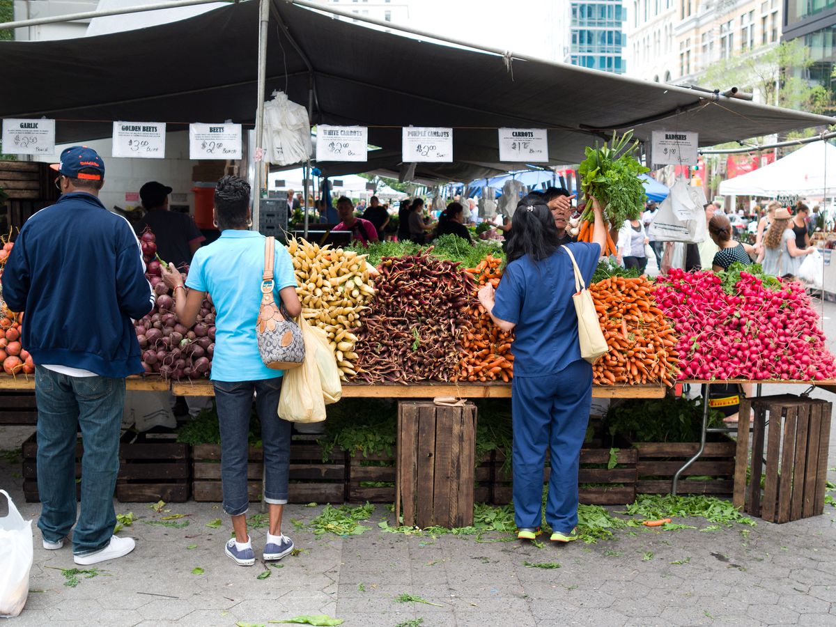Customers shop through piles of fresh produce (like potatoes and carrots) at the Union Square Greenmarket in Manhattan, New Yorjk City. 
