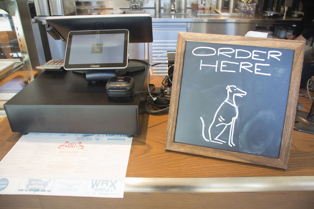 A cash register with a chalkboard sign of a dog and words that read “Order Here.”