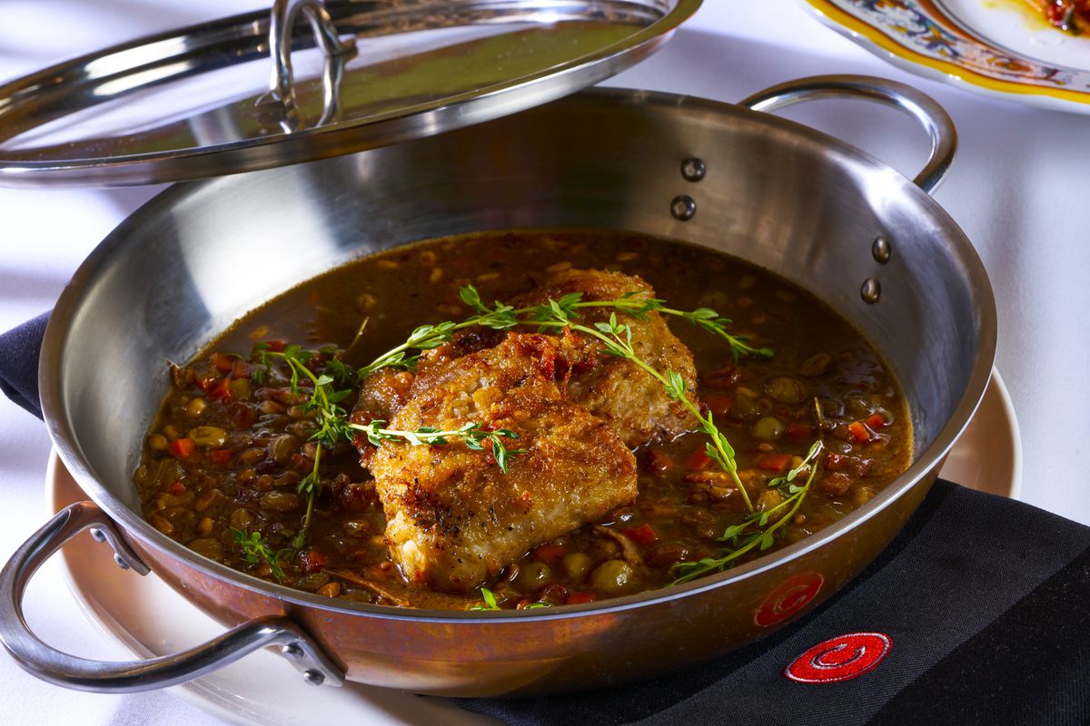 In a metal pan, cooked rabbit is surrounded by a cherry sauce and covered in rosemary.