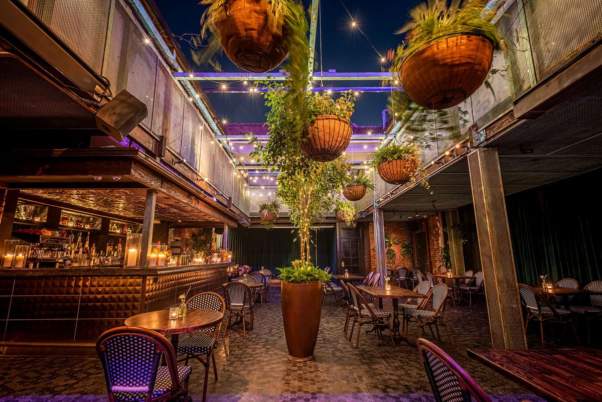 Bar and dining areas with open air, hanging plants, hanging lights, and bar to the left at Fingers Crossed in Hollywood.