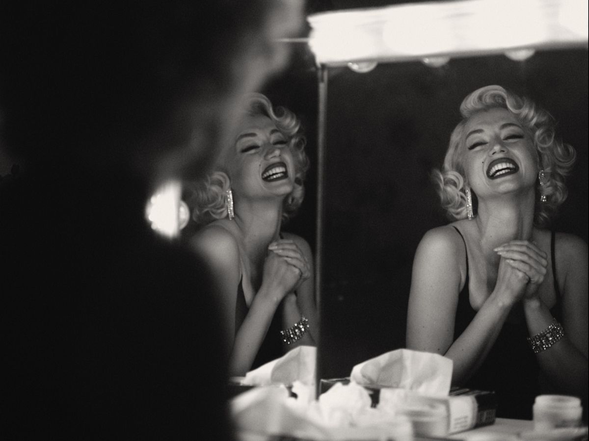 Ana de Armas as Marilyn Monroe smiles, reflected in two mirrors in black and white