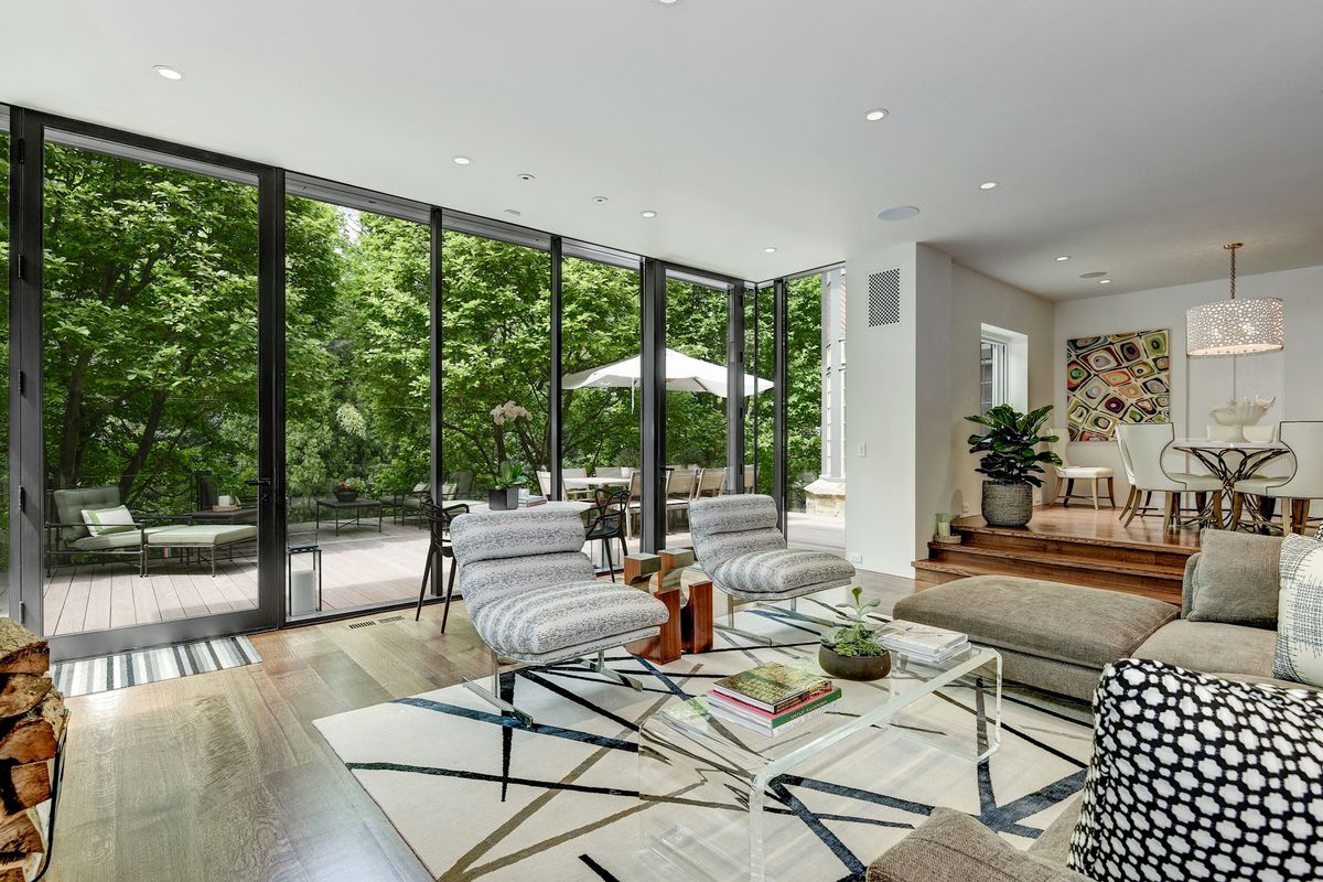 A living room has seating and a glass coffee tabe in front of floor-to-ceiling glass walls. 