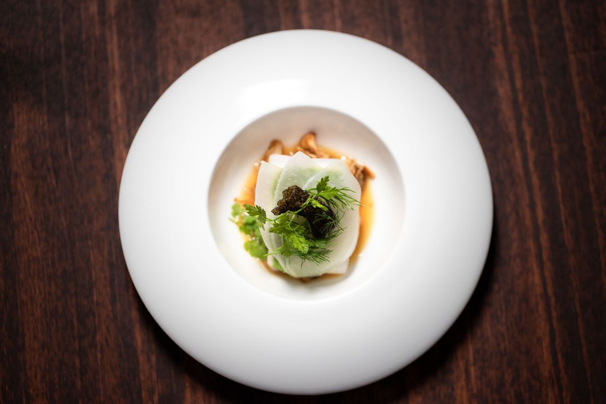 Top-down view of black cod with matsutake mushroom, turnups, and dill on a white plate.