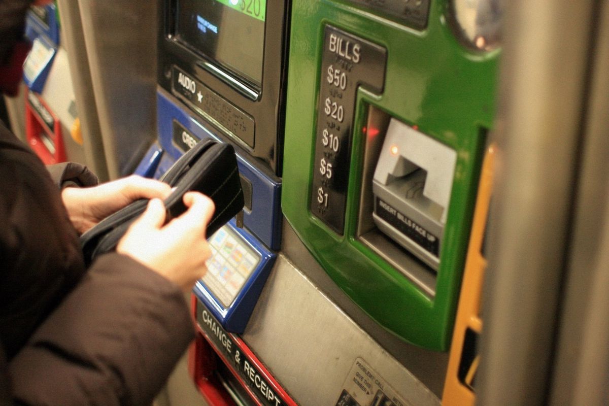 A person in front of a subway vending machine, opening their wallet.