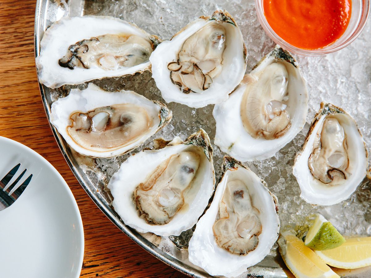 A close-up photos of oysters on ice with a red sauce in the center of the circular tray.