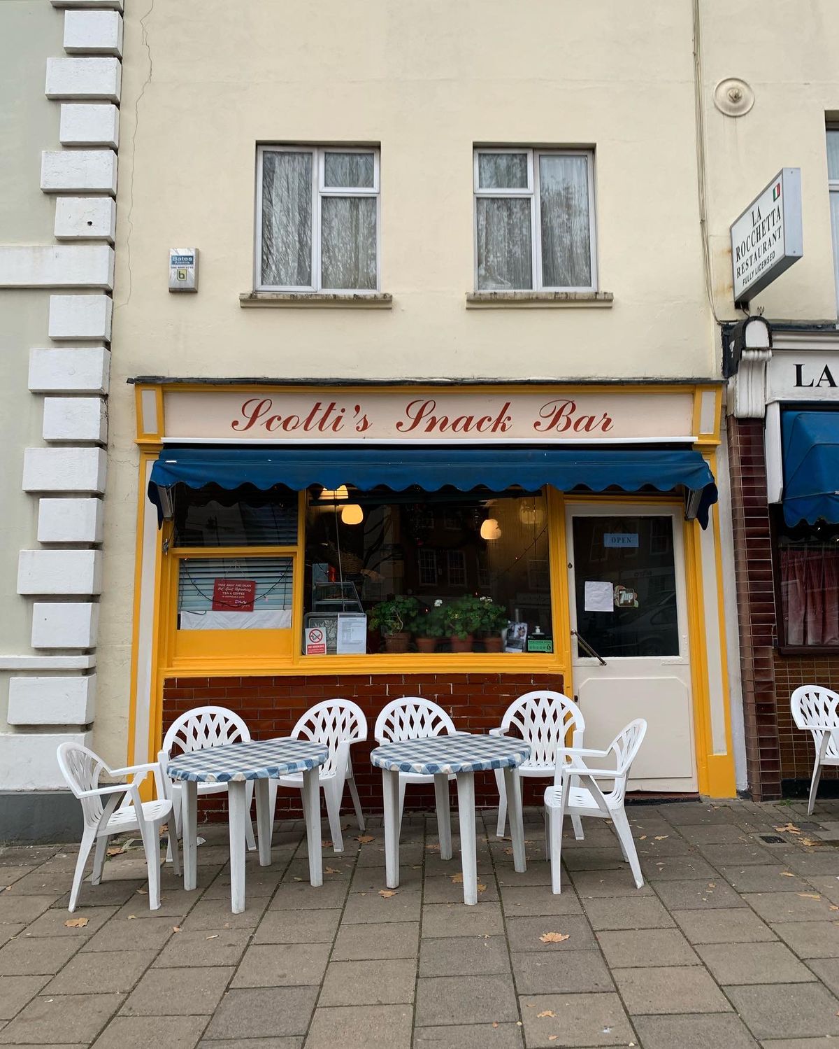 Scotti’s Snack Bar — the blue cream and yellow caff in Clerkwenwell Green has white plastic tables and chairs outside on concrete flagstones.