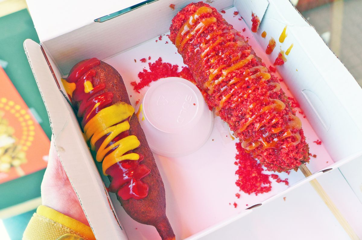 Two corn dogs covered in sauces in a box.