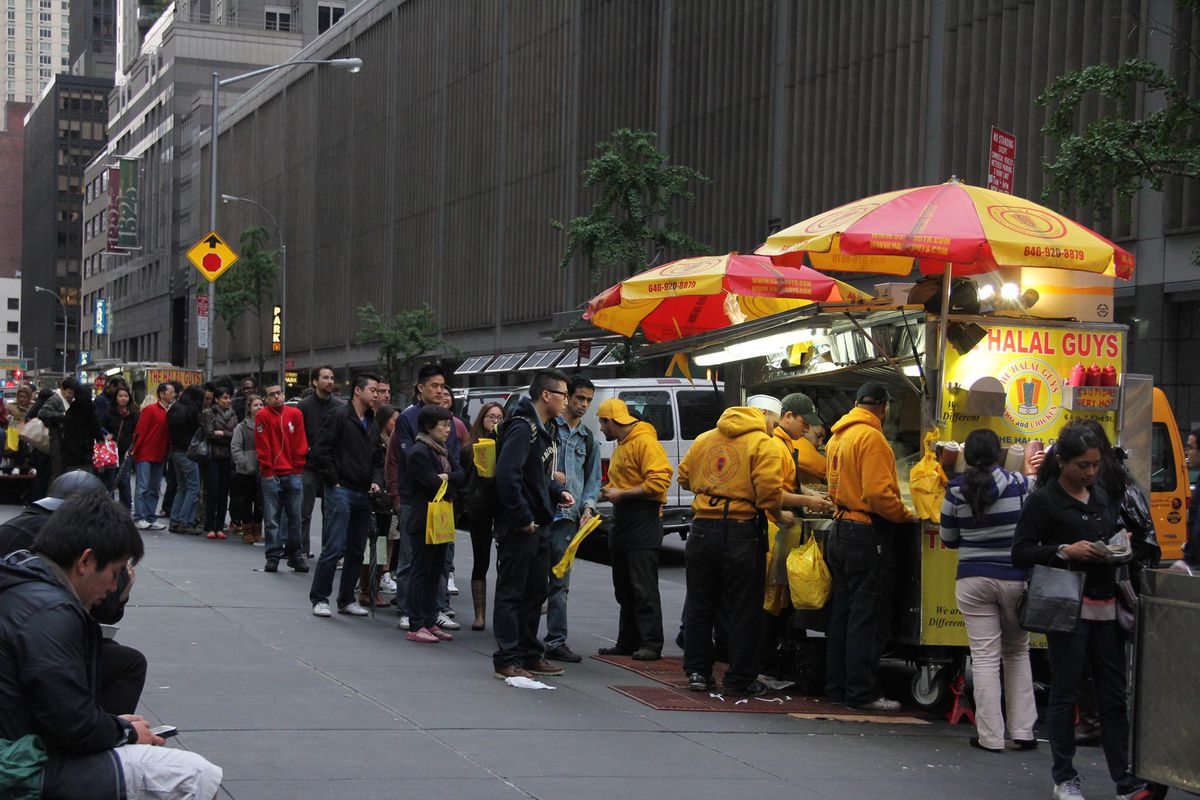 A line forms down the street at a location of Halal Guys.