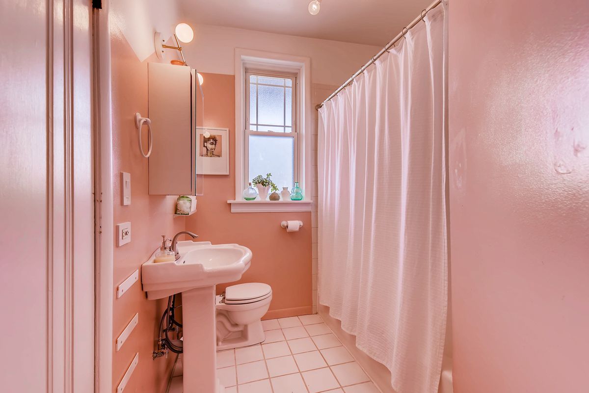 The bathroom has a white shower curtain, a white pedestal sink, and white tiles on the floor. The rest of the walls are painted pink.