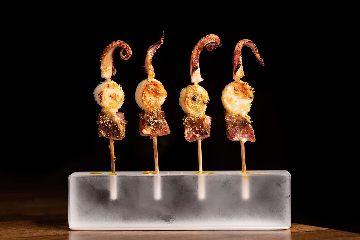 Skewers with seafood stick out from a clear block.