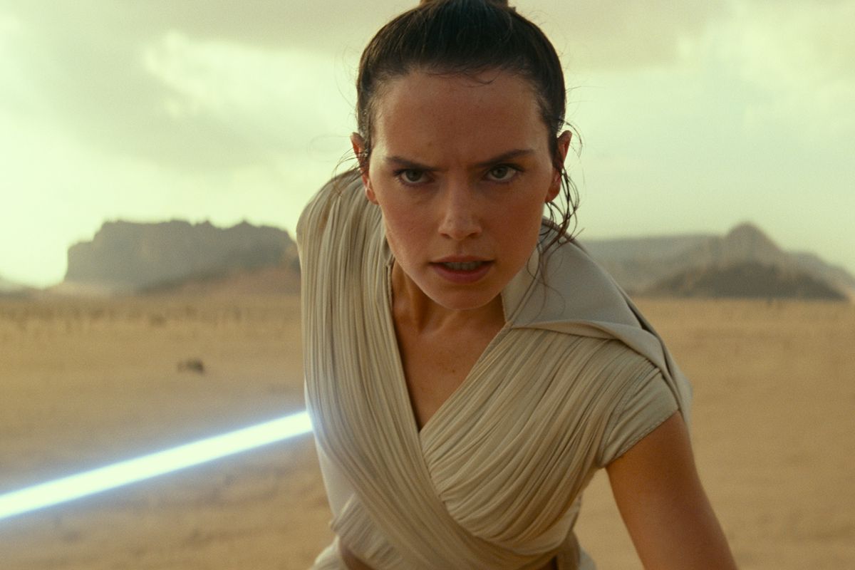 rey stands in a battle stance with luke’s lightsaber