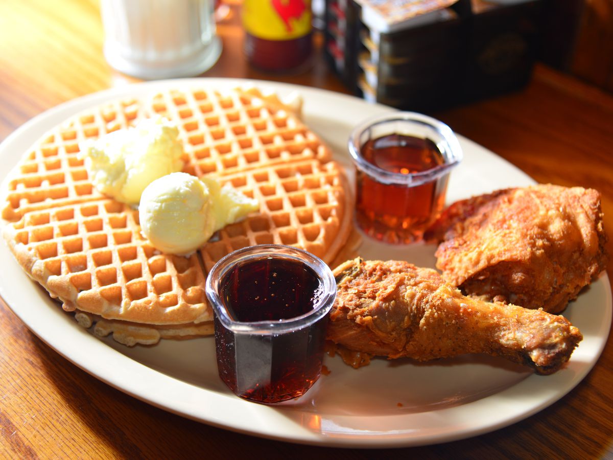 Big pats of butter sit on top of golden waffles, with maple syrup and fried chicken on the side