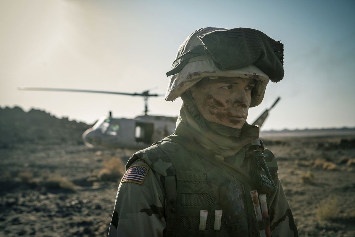 Muddy Tom Holland in Army gear in Iraq standing in front of a helicopter