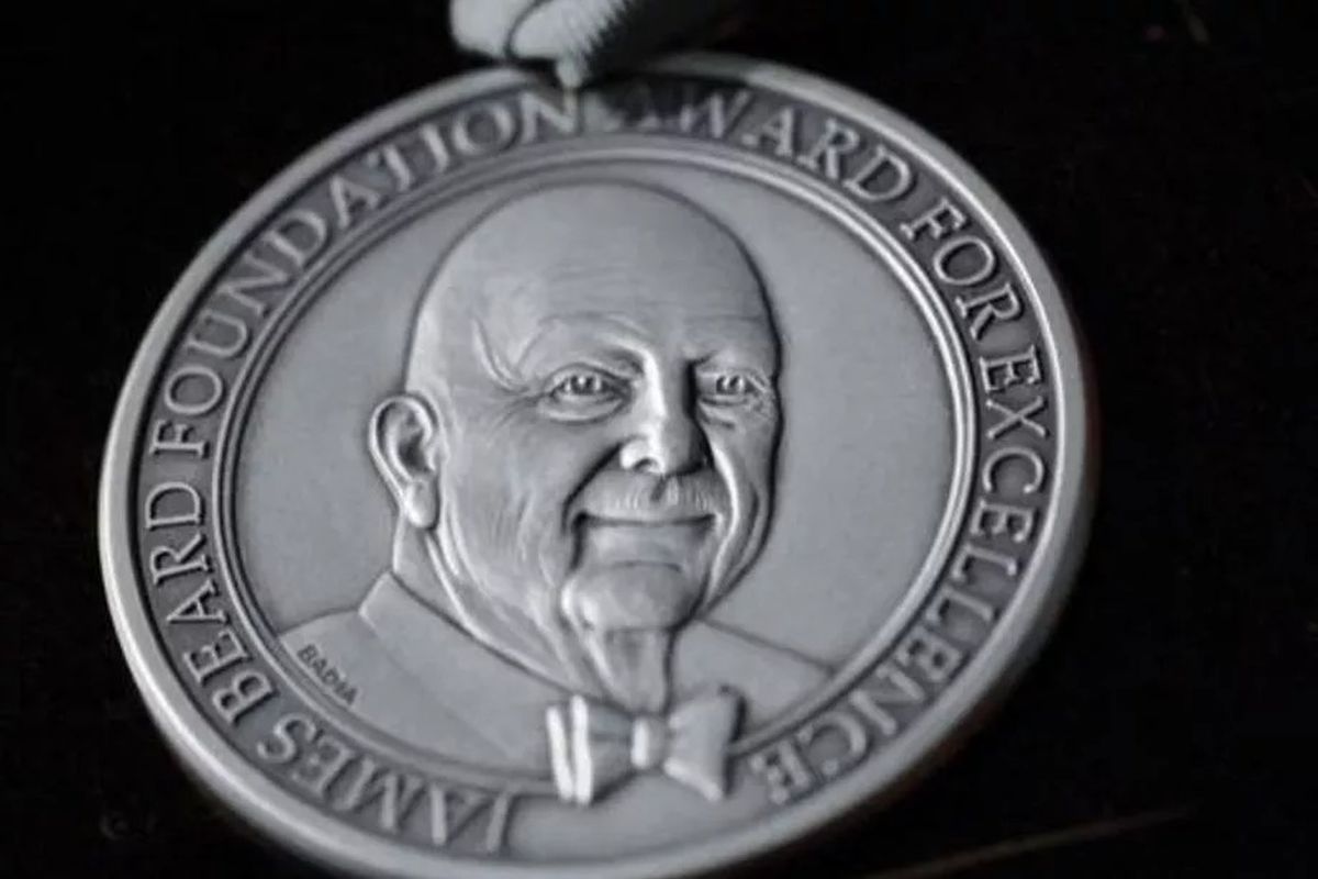A silver medallion with a portrait of famous cookbook author James Beard wearing a bow tie
