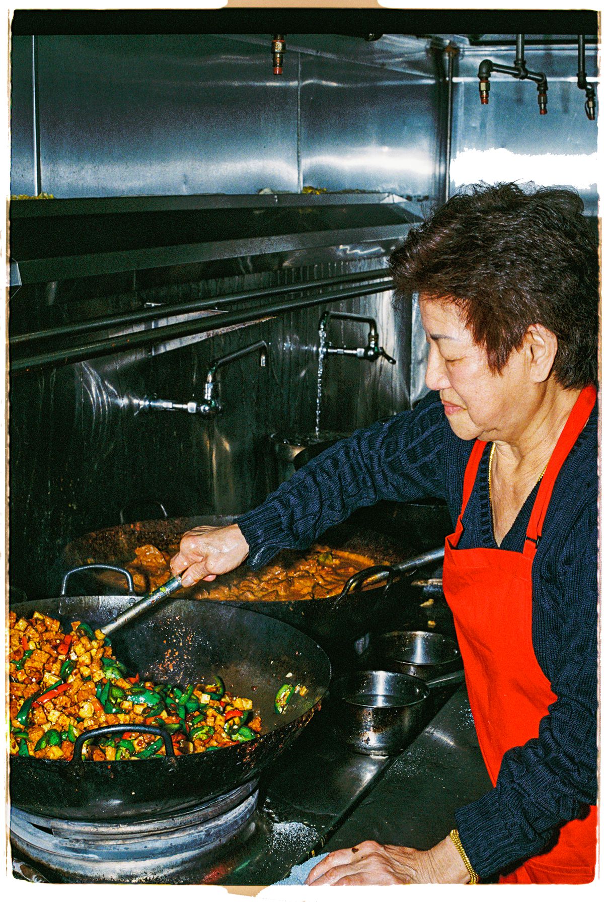 A woman wearing an apron cooks food on a wok.
