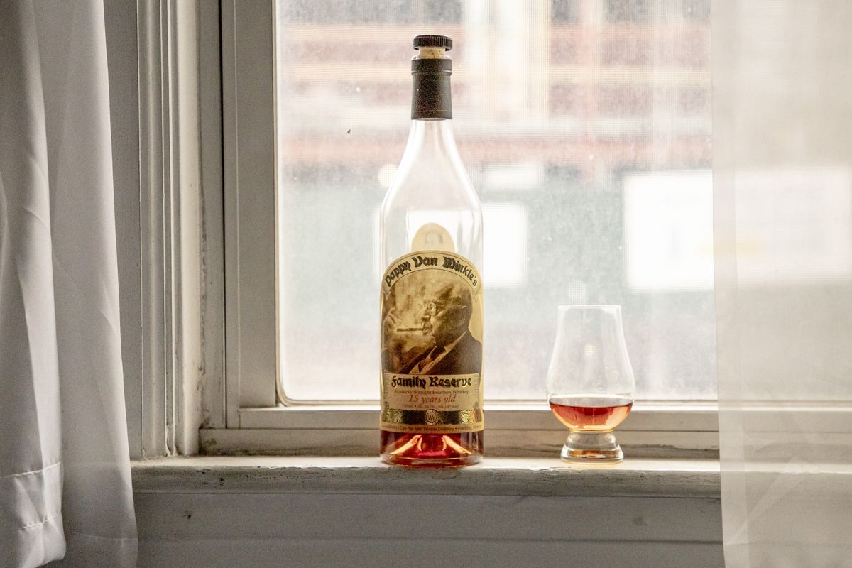 A bottle of Pappy Van Winkle in a window, next to a glass filled with a little bit of bourbon.