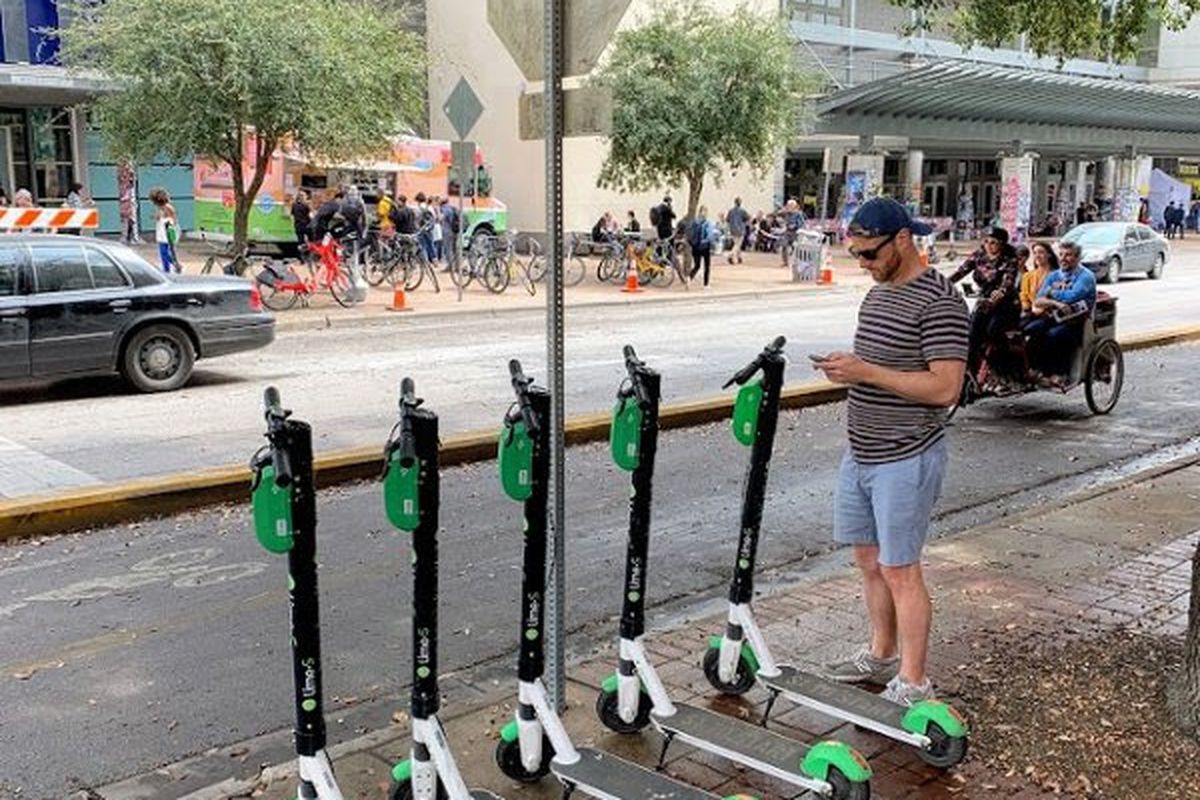 Man with phone standing by Lime scooters on sidewalk