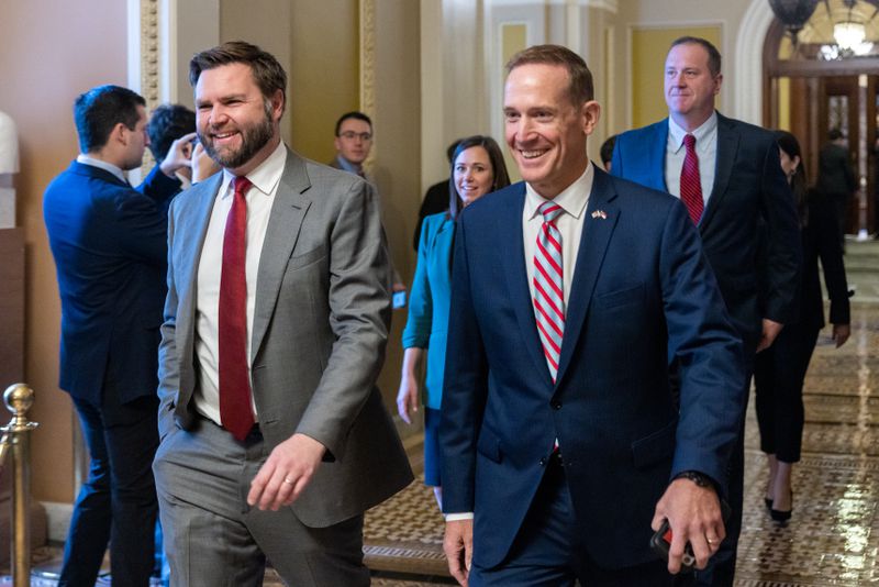 JD Vance and Ted Budd smile as they walk side-by-side through a hallway featuring arched doors and a gold and brown tile mosaic floor.