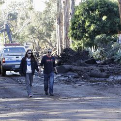 A woman and man walk along a road damaged by storms in Montecito, Calif., Wednesday, Jan. 10, 2018. Dozens of homes were swept away or heavily damaged and several people were killed Tuesday as downpours sent mud and boulders roaring down hills stripped of vegetation by a gigantic wildfire that raged in Southern California last month. (AP Photo/Marcio Jose Sanchez)