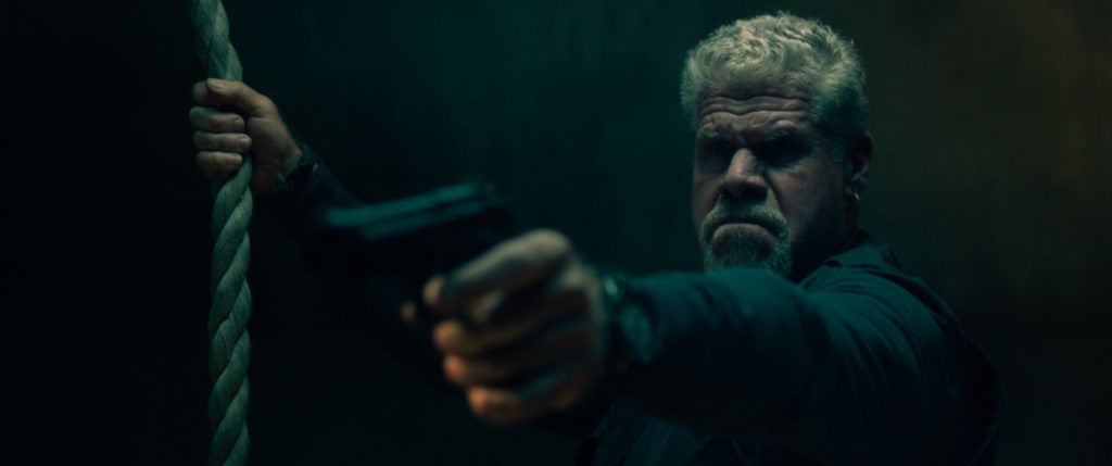 Ron Perlman aiming a gun and holding a rope in There Are No Saints.