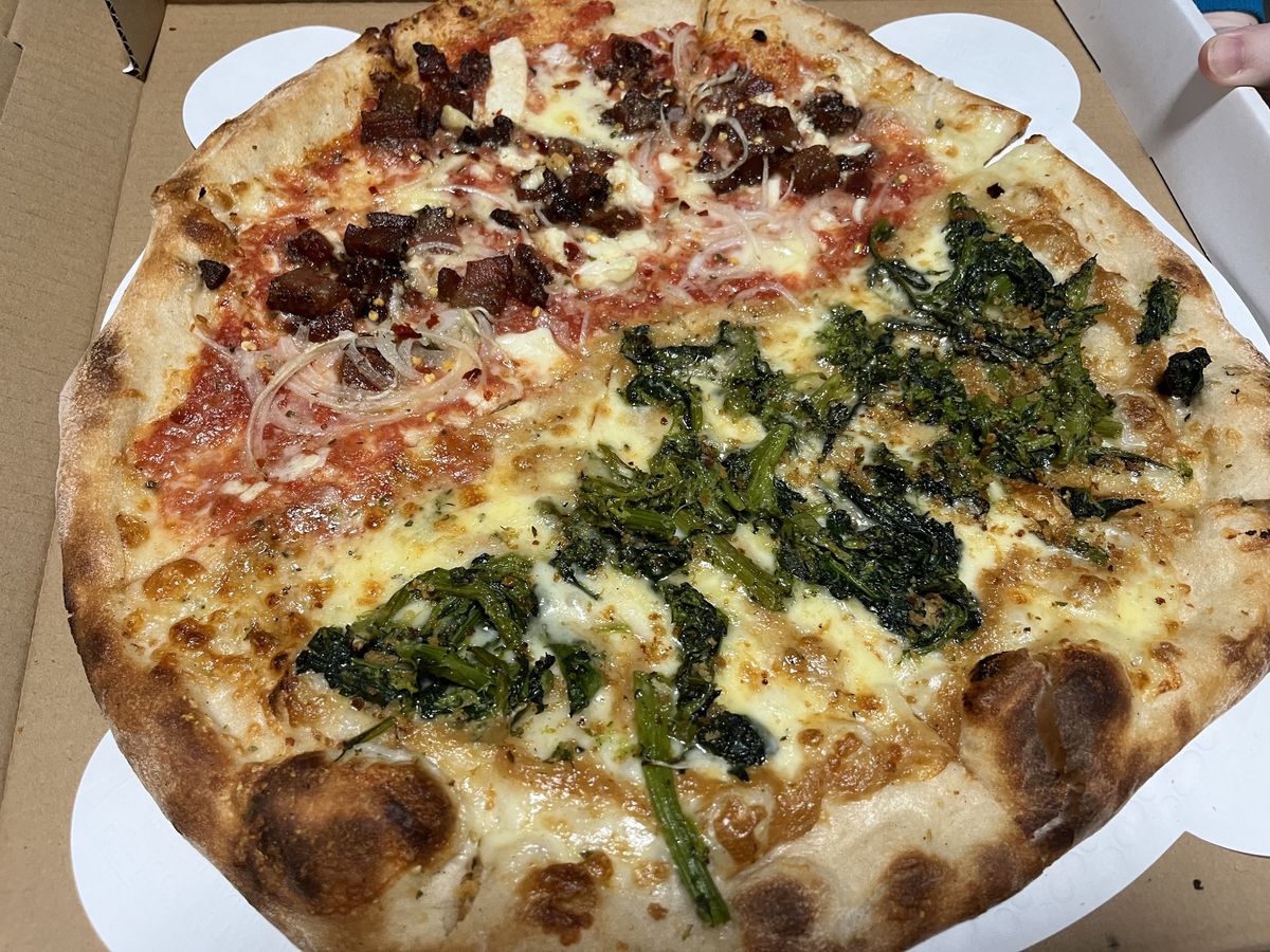 A pizza that has meat toppings on one half and broccoli on the other.